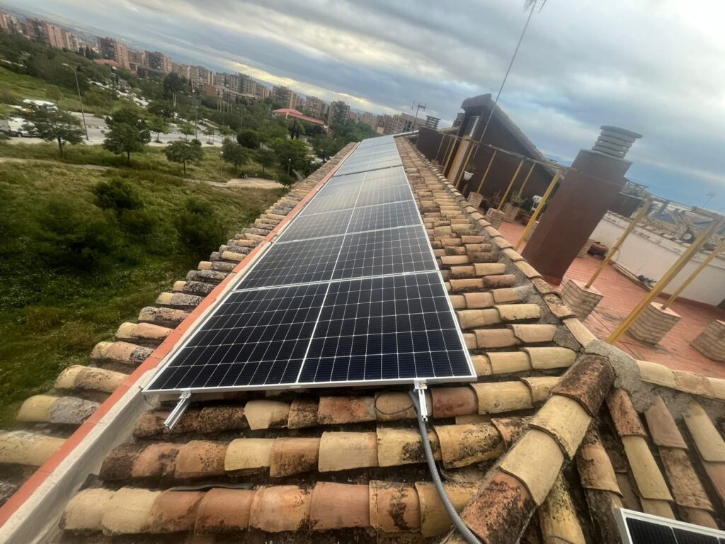 Módulos fotovoltaicos instalados a lo largo de un tejado de teja con zona verde al fondo Módulos fotovoltaicos instalados a lo largo de un tejado de teja con zona verde al fondo