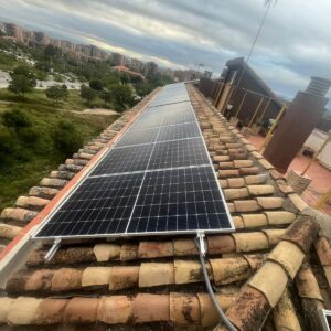 Módulos fotovoltaicos instalados a lo largo de un tejado de teja con zona verde al fondo