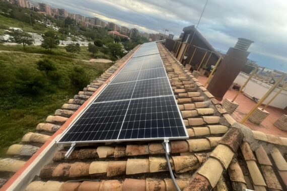 Módulos fotovoltaicos instalados a lo largo de un tejado de teja con zona verde al fondo