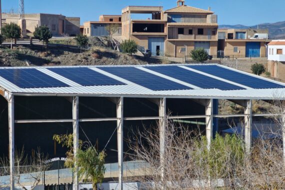 Cubierta fotovoltaica sobre la estructura de un frontón municipal con el pueblo de montaña al fondo Cubierta fotovoltaica sobre la estructura de un frontón municipal con el pueblo de montaña al fondo