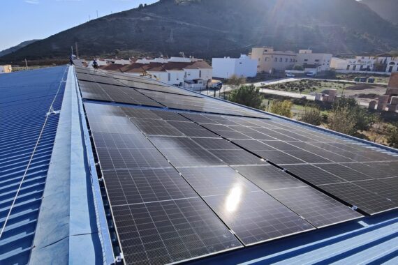 Campo fotovoltaico sobre cubierta de chapa de un edificio municipal con la sierra al fondo Campo fotovoltaico sobre cubierta de chapa de un edificio municipal con la sierra al fondo