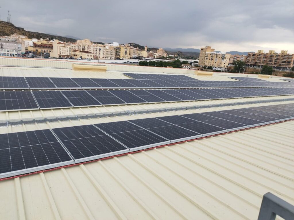 Filas de módulos fotovoltaicos sobre la cubierta de chapa de un supermercado con la ciudad al fondo Filas de módulos fotovoltaicos sobre la cubierta de chapa de un supermercado con la ciudad al fondo