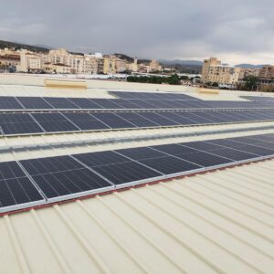 Filas de módulos fotovoltaicos sobre la cubierta de chapa de un supermercado con la ciudad al fondo