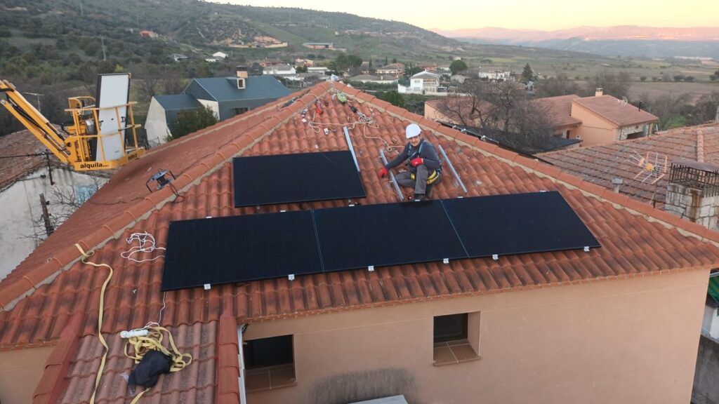 Montaje de módulos fotovoltaicos sobre tejado de teja con operario con arnés y la sierra al atardecer Montaje de módulos fotovoltaicos sobre tejado de teja con operario con arnés y la sierra al atardecer