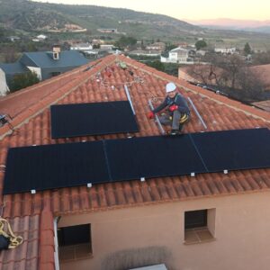 Montaje de módulos fotovoltaicos sobre tejado de teja con operario con arnés y la sierra al atardecer