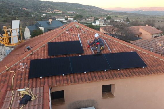Montaje de módulos fotovoltaicos sobre tejado de teja con operario con arnés y la sierra al atardecer